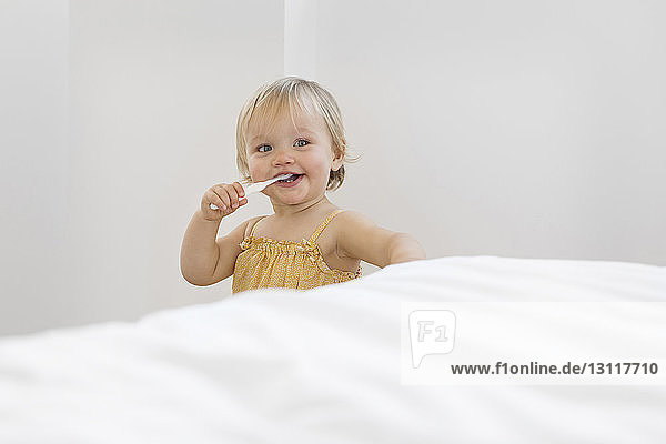 Süßes Mädchen putzt zu Hause am Bett stehend die Zähne