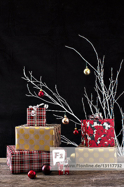 Weihnachtsgeschenke mit Dekoration auf Holztisch vor schwarzem Hintergrund
