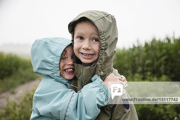 Glückliche Schwester umarmt Bruder  während sie in der Regenzeit gegen Pflanzen steht