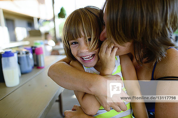 Mutter küsst und umarmt glückliche Tochter  während sie am Tisch im Hof sitzt