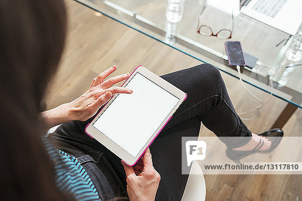 Hochwinkelansicht einer Geschäftsfrau  die einen Tablet-Computer benutzt  während sie im Büro sitzt