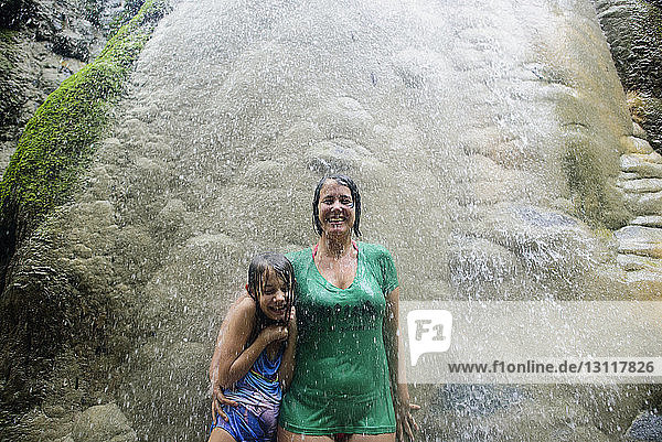 Happy woman with daughter standing by rocks at Bua Thong Waterfalls