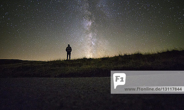 Mann steht nachts gegen Sternenfeld