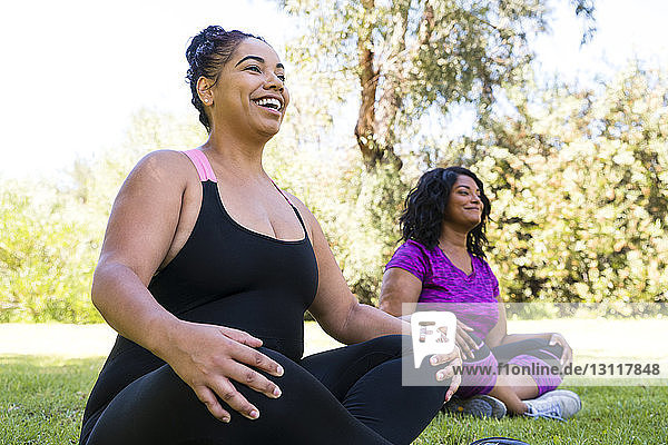 Niedriger Blickwinkel auf glückliche Freundinnen  die meditieren  während sie im Park sitzen