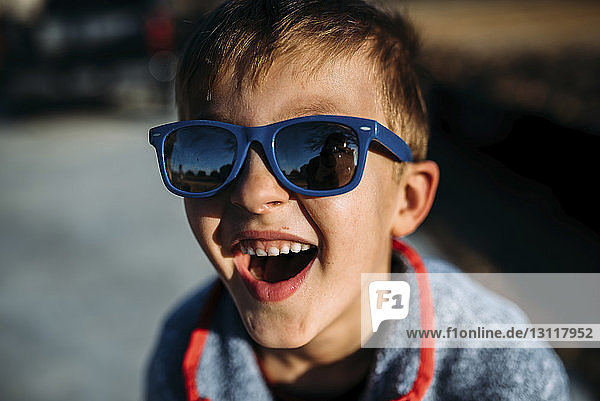 Hochwinkel-Nahaufnahme eines glücklichen Jungen  der eine Sonnenbrille trägt  während er im Freien sitzt