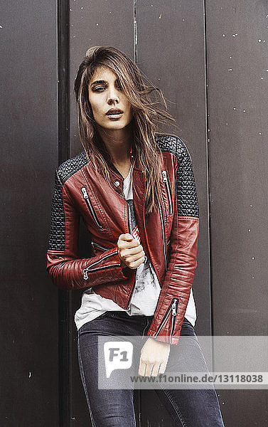 Portrait of young woman wearing leather jacket standing against wall