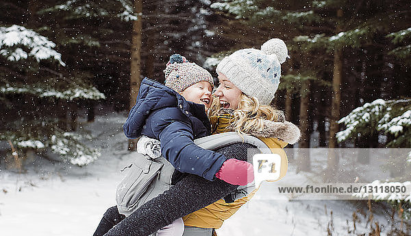 Glückliche Mutter trägt Tochter im Winter im Wald