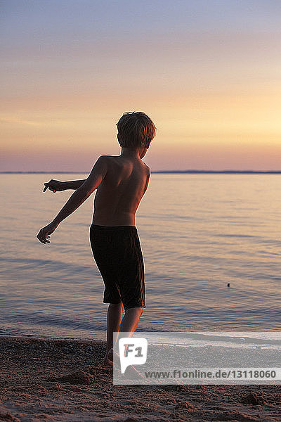 Rückansicht eines Jungen  der am Strand einen Stein ins Wasser wirft