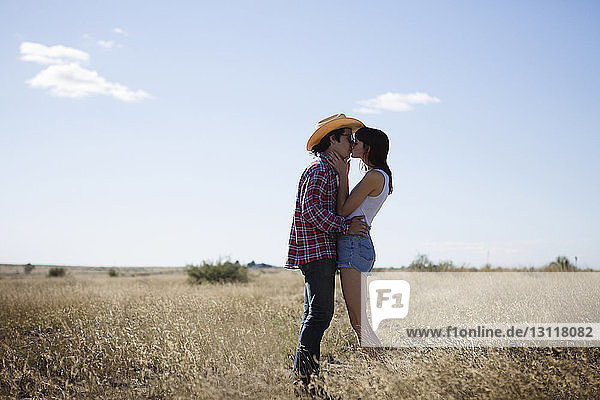 Seitenansicht eines Paares  das sich auf dem Feld gegen den Himmel küsst