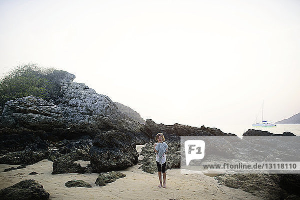 Full length of girl standing on sand by rocks at beach against sky
