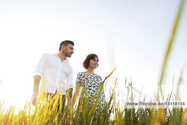Low angle view of man standing with PRegnant woman on grassy field against clear sky