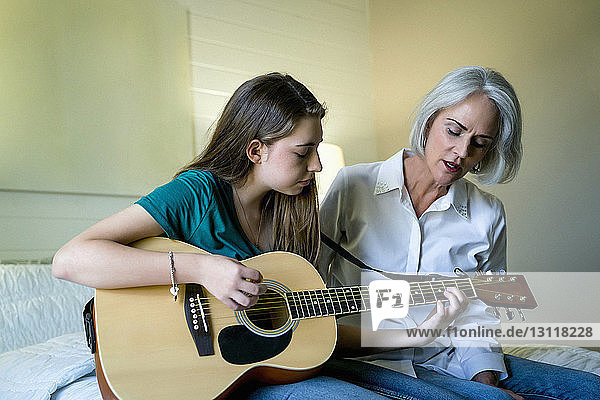 Enkelin spielt Gitarre  während sie bei der Großmutter im Schlafzimmer sitzt