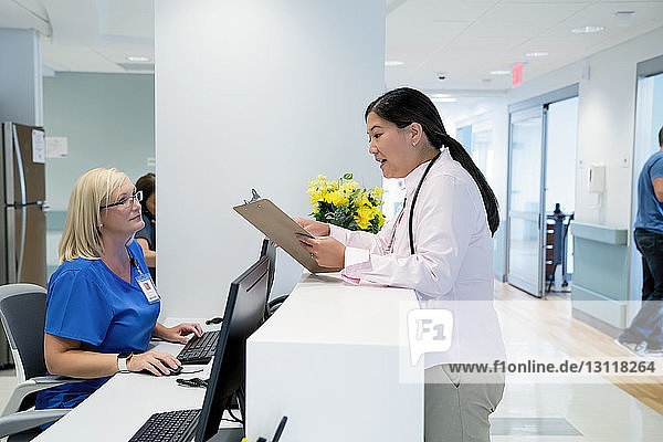 Female doctor looking at clipboard while talking with nurse at hospital reception