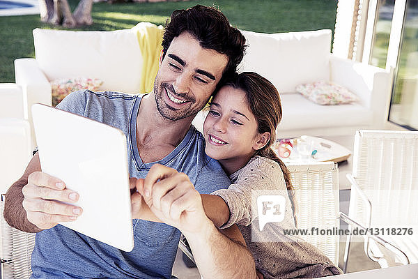 Glücklicher Vater und Tochter benutzen digitales Tablet  während sie auf einem Stuhl sitzen