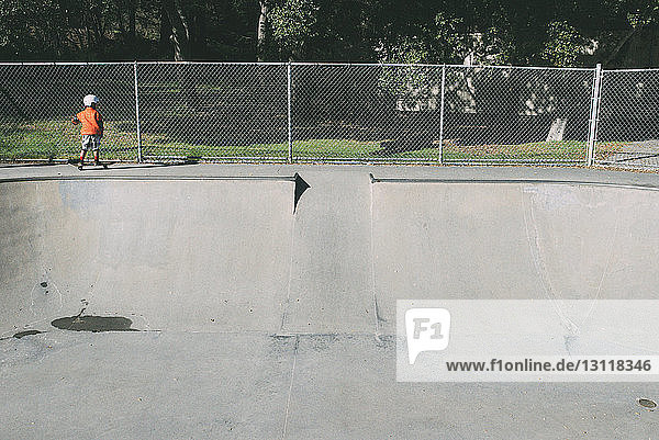 Rückansicht eines Jungen im Skateboard-Park gegen einen Zaun