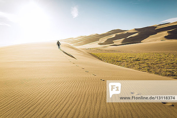 Rückansicht eines sorglosen Mannes  der bei Sonnenschein im Great Sand Dunes National Park auf Sand läuft