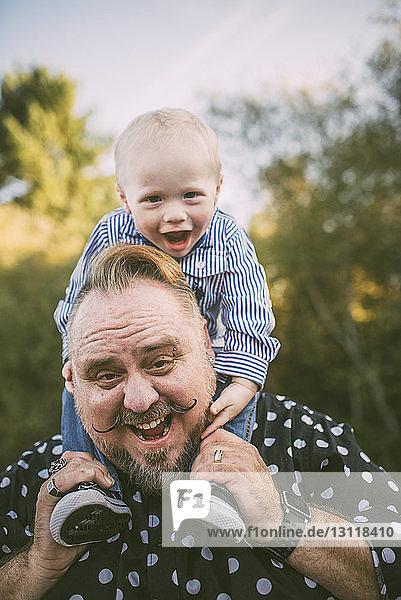 Portrait of cheerful father carrying cute son on shoulders at park