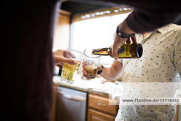 Midsection of man poring beer for friend while standing in kitchen