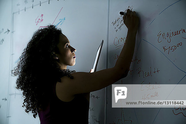 Geschäftsfrau schreibt im Büro auf Whiteboard über Tablet-Computer