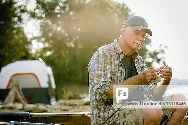 Älterer Mann stellt Angelgeräte ein  während er auf dem Boot gegen Bäume sitzt