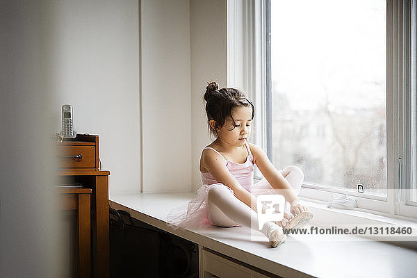 Mädchen in Ballettschuhen  das zu Hause am Tisch am Fenster sitzt