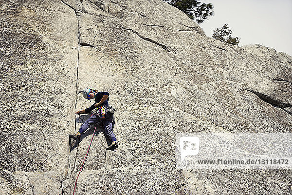 Low angle view of woman adjusting rope while climbing mountain