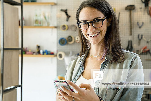 Porträt einer glücklichen Geschäftsfrau mit Smartphone im Büro