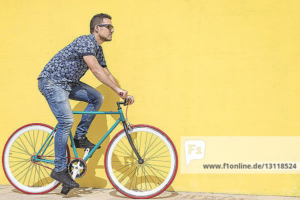 Mann fährt Fahrrad gegen gelbe Wand am Bürgersteig in der Stadt