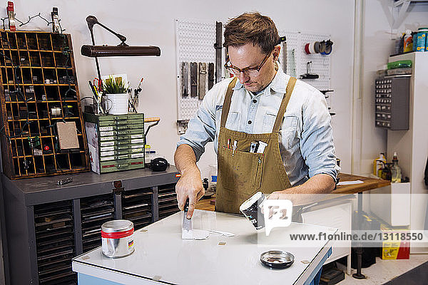 Konzentrierter Mann streicht bei der Arbeit in der Druckerpresse Farbe auf den Tisch