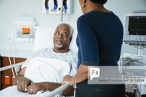 Vater sieht Tochter an  während er sich auf der Krankenhausstation ans Bett lehnt