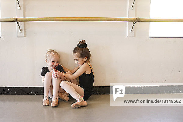 Verspieltes Mädchen kitzelt Freundin beim Sitzen im Ballettstudio