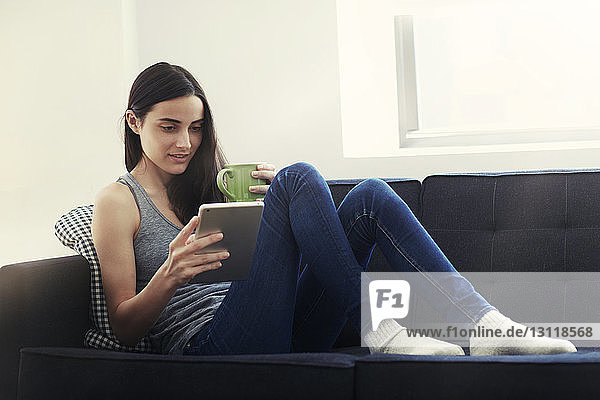 Frau sitzt auf dem Sofa und benutzt ein digitales Tablet