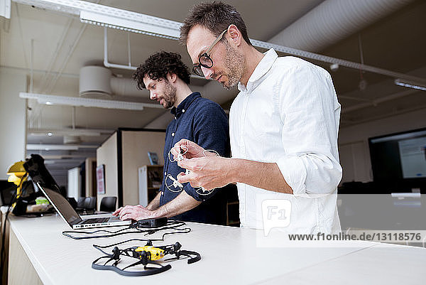 Technician examining drone while coworker using laptop computer at table in office