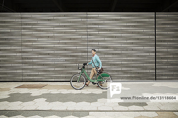 Side view of mature man walking with bicycle on footpath by wall