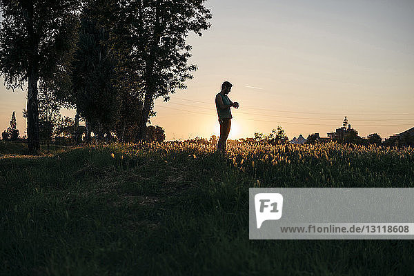 Mann untersucht Spurenleser  während er bei Sonnenuntergang auf einem Grasfeld vor klarem Himmel steht