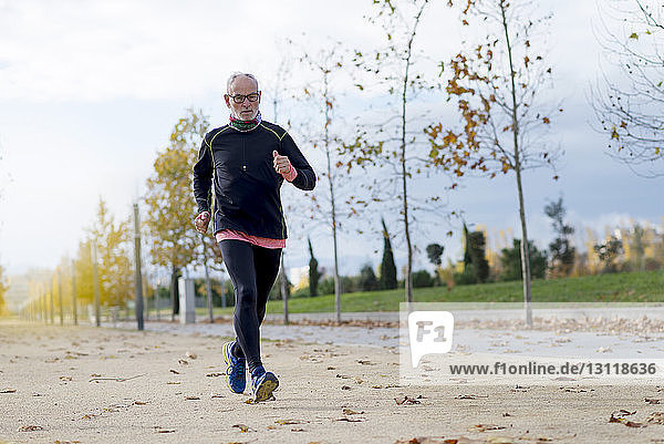 Joggen eines älteren Mannes in voller Länge  während er im Herbst im Park trainiert