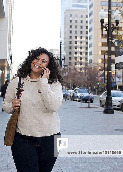 Lächelnde Frau telefoniert in der Stadt auf dem Bürgersteig