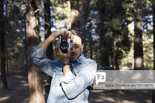 Mann fotografiert mit Kamera gegen Bäume im Wald