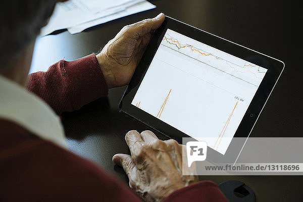 Ausgeschnittenes Bild eines hochrangigen Mannes  der eine Grafik auf einem Tablet-Computer im Büro eines Finanzberaters untersucht