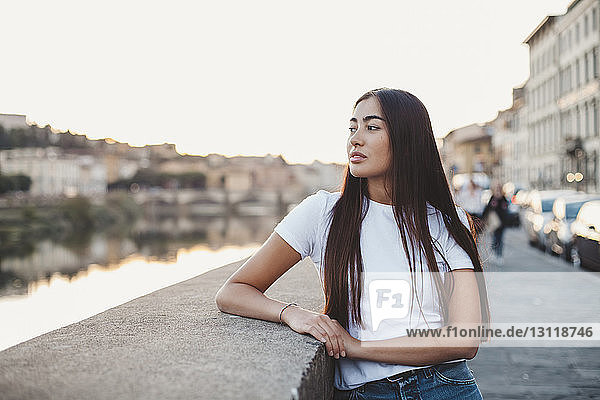 Nachdenkliche junge Frau schaut weg,  während sie am Kanal in der Stadt steht