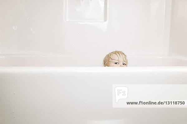 Portrait of boy peeking while sitting in bathtub
