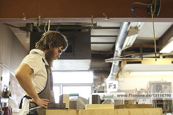 Seitenansicht eines Tischlers mit der Hand auf der Hüfte stehend an der Werkbank in der Werkstatt