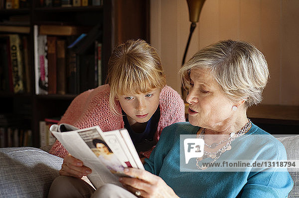 Grandmother reading magazine while sitting on sofa at home