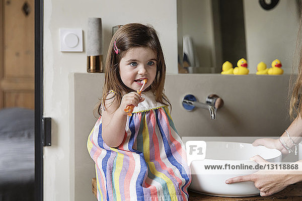 Abgehackte Hände der Mutter halten Waschbecken  während die Tochter zu Hause im Badezimmer Zähne putzt