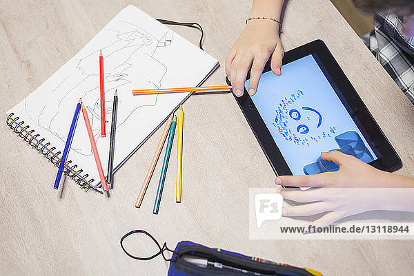 Hochwinkelansicht eines Jungen  der auf einem Tablet-Computer am Tisch zeichnet