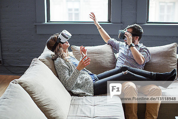 Mitarbeiter tragen Virtual-Reality-Simulatoren  während sie im Büro auf dem Sofa sitzen