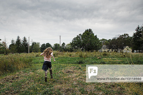 Rear view of girl running on grassy field against cloudy sky