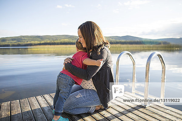 Loving son embracing pregnant mother on wooden pier over lake