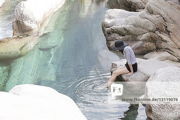 Seitenansicht einer Wanderin  die mit den Füßen im Fluss auf einem Felsen sitzt