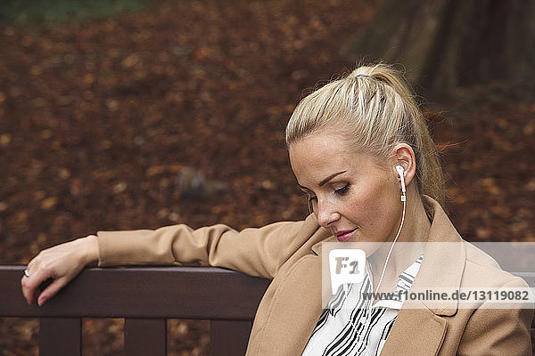 Nahaufnahme einer Frau  die im Herbst auf einer Parkbank sitzend Musik hört